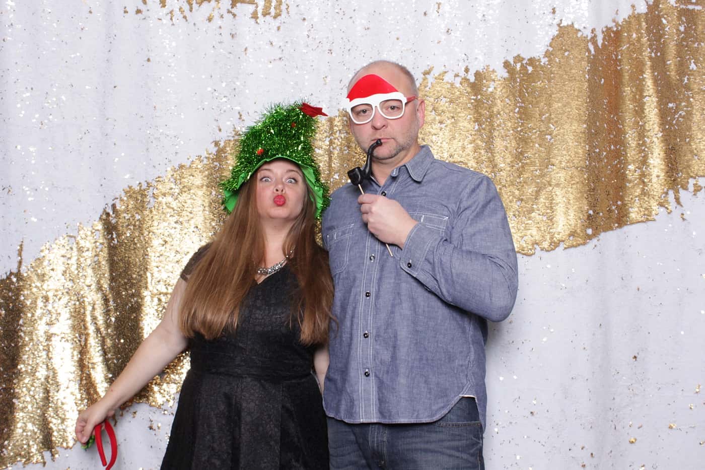 company christmas party photo booth photo taken against a white and gold sequin backdrop with christmas props