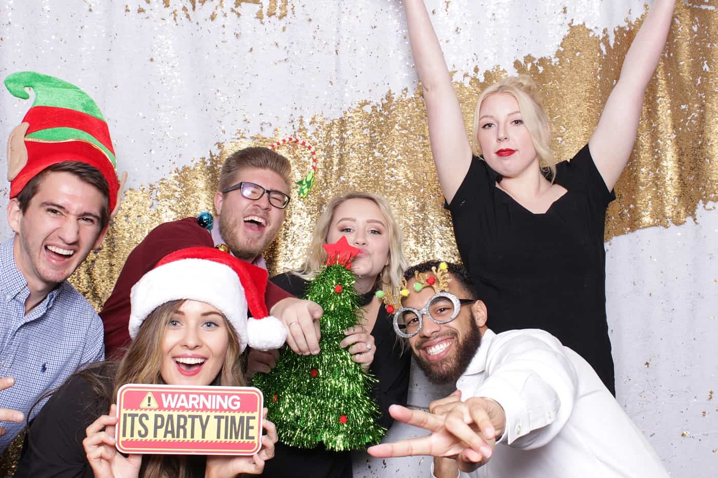 company christmas party photo booth photo taken against a white and gold sequin backdrop with christmas props